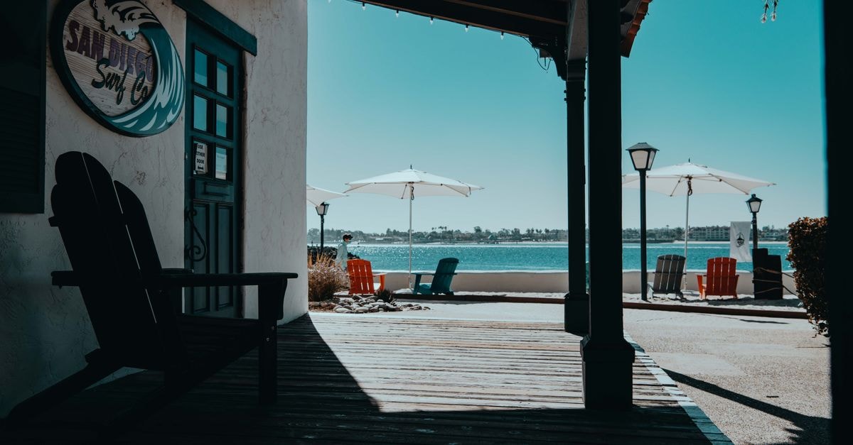 San Diego Travel Guide: Coastal Calm Year-Round A serene beachfront view with shadows on a wooden deck and umbrellas by the water.