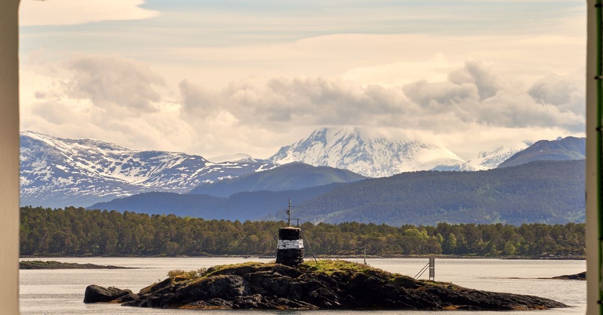 Molde Travel Guide: Fjord Views, Roses, and Quiet Norwegian Charm Breathtaking view of snowcapped mountains and a small island seen from a window in Molde, Norway.