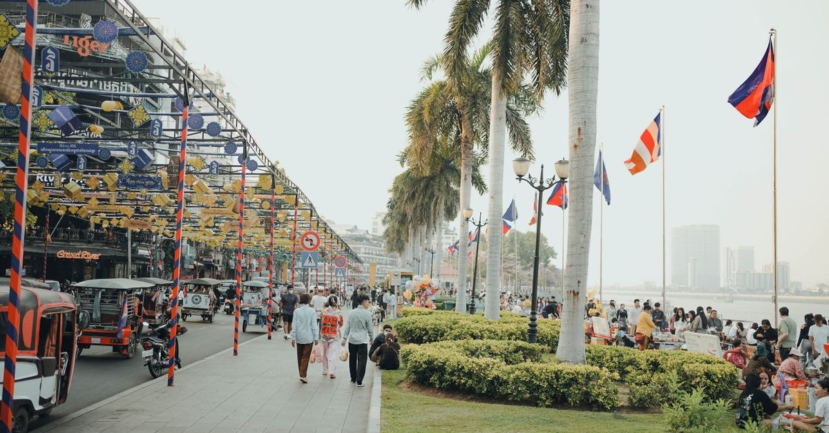 Phnom Penh Travel Guide: A Slow, Flavor-First Way Into the City Bustling scene along Phnom Penh riverside with tuk-tuks, people, and flags creating a lively atmosphere.