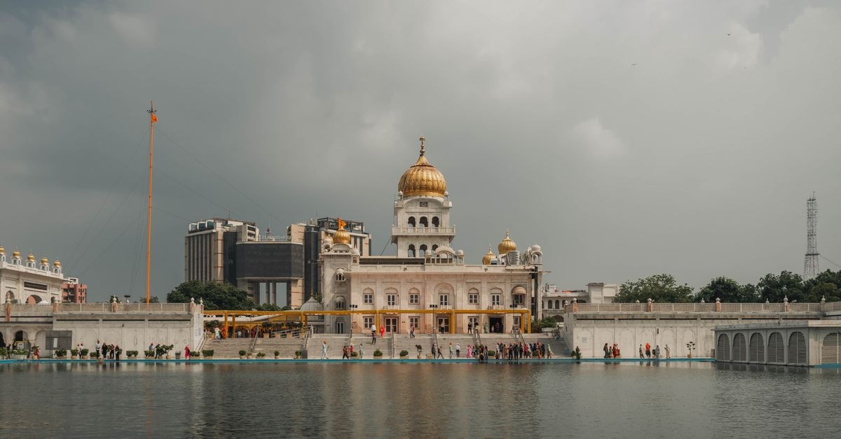 Stunning view of Gurudwara Bangla Sahib with reflection on the water under a cloudy sky in Delhi.