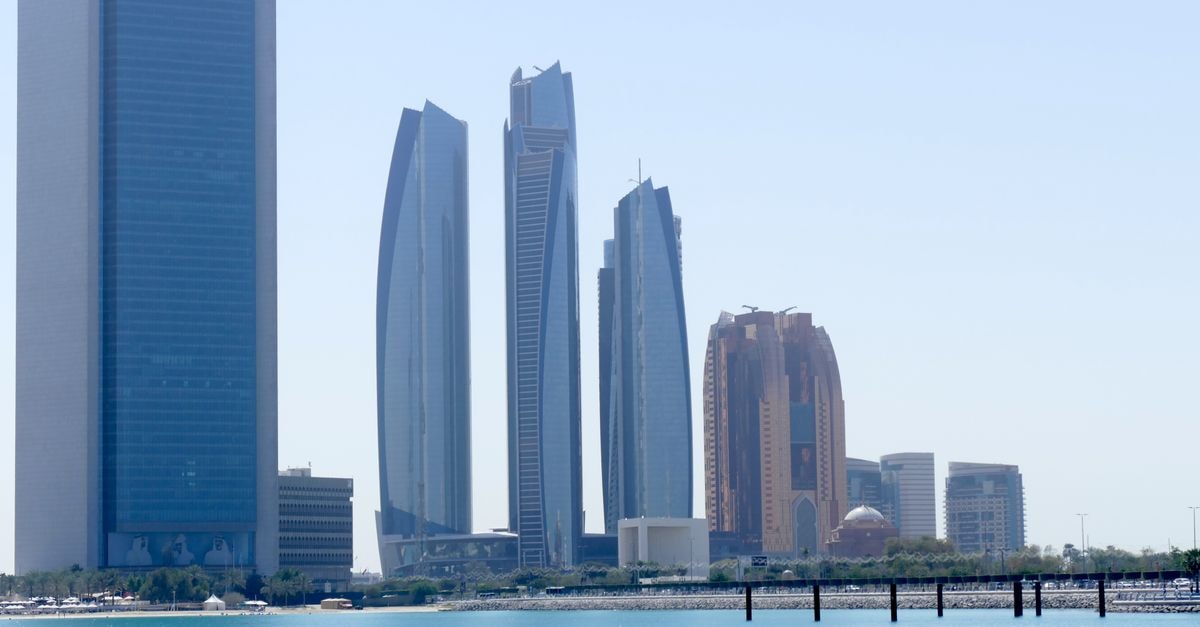 View of Abu Dhabi skyline with modern skyscrapers reflecting over the calm water.