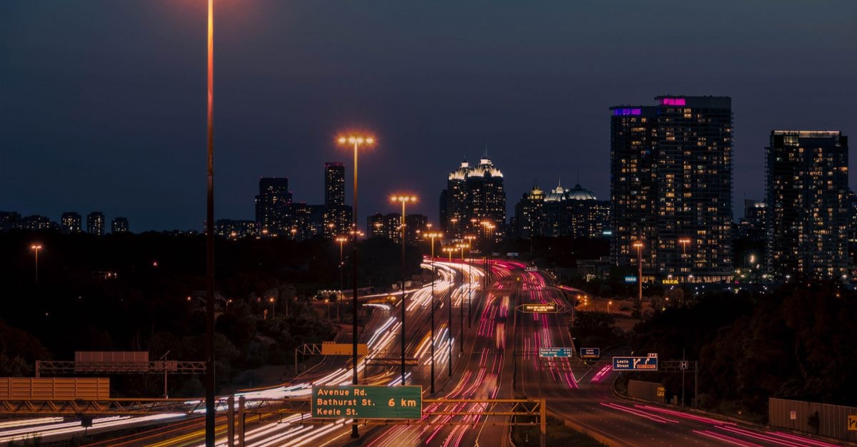Vibrant light trails on a Toronto highway with city skyline at dusk, capturing urban energy.