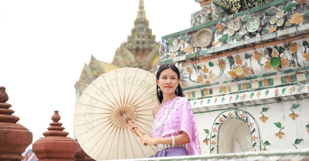 Lopburi Travel Guide: Palaces, Prangs and Practical Local Tips A woman in traditional Thai dress poses with a parasol at Wat Arun temple in Bangkok, Thailand.