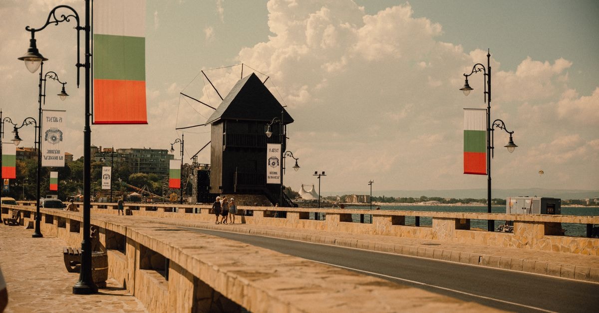 Targovishte Travel Guide: A Quiet Bulgarian Revival Town Worth a Stop Vintage-style photo of a coastal road with a historic windmill and national flags.
