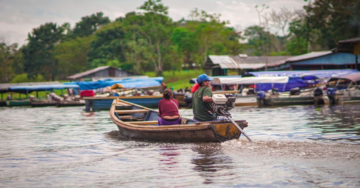 Zamora Travel Guide: Amazon Flavors and Highland Soul A man and woman navigating a motorboat on the Amazon River near Leticia, Colombia. Vibrant waterway scene.