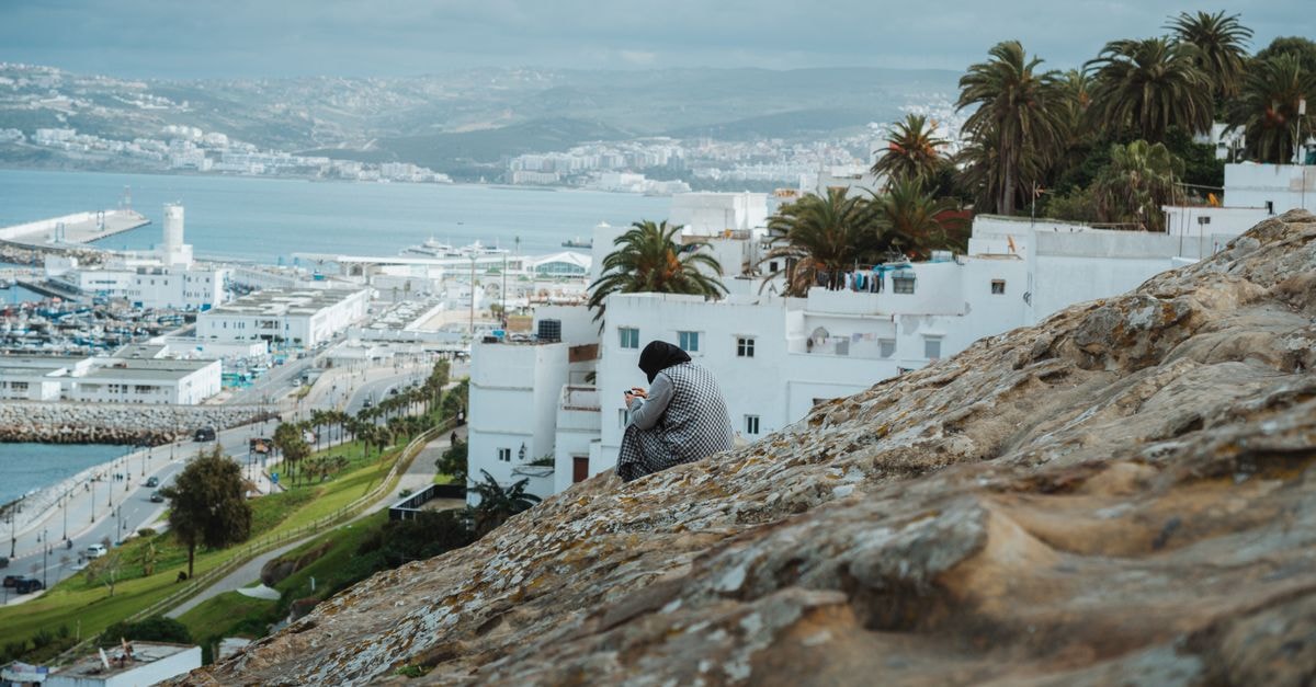 Hotel Kamal City Center, Agadir — A Pool and Sundeck on Hassan II Boulevard Woman sitting on hill overlooking Tangier port, capturing urban landscape.