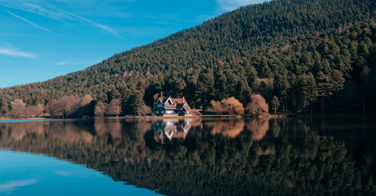 Ioannina Travel Guide: Lake Reflections and Mountain Calm Idyllic lakeside view with reflection of a house and forested hills in Bolu, Türkiye.