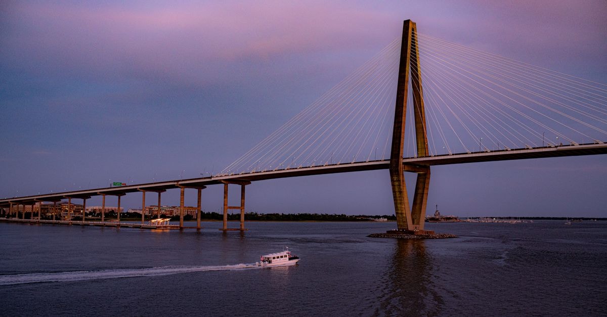 Scenic view of Charleston's Arthur Ravenel Jr. Bridge at sunset with a boat on the water.