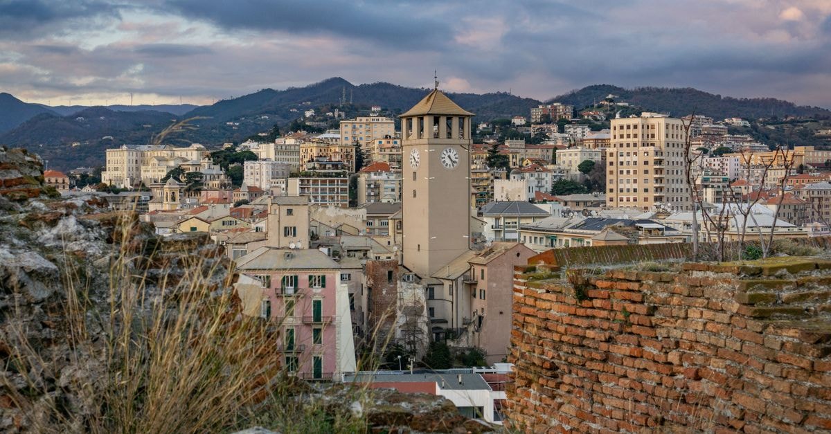 View of Savona's Torre del Brandale surrounded by picturesque cityscape and hills at dusk.