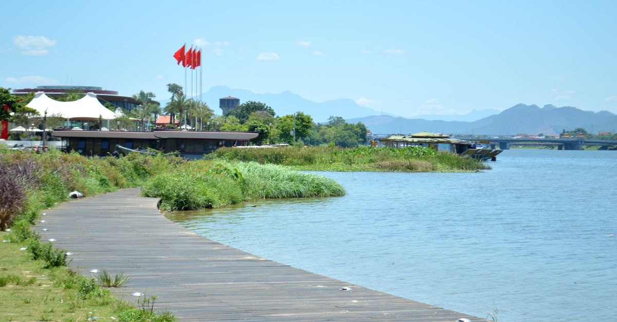 Zhenjiang Travel Guide: River Views and a Slow Food Rhythm Serene riverside scene with boardwalk, flags, and distant mountains under a bright blue sky.