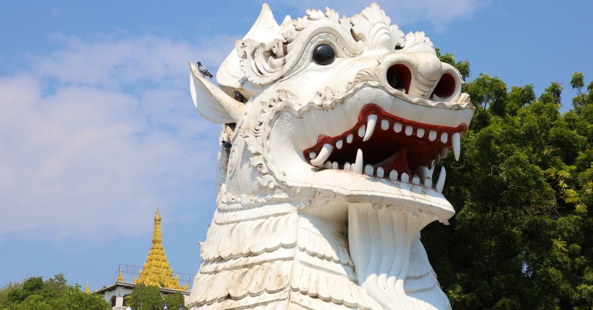Mandalay travel guide: a slow look at Myanmar's royal city Intricately carved white chinthe statue with golden pagoda in the background at Mandalay Hill, Myanmar.
