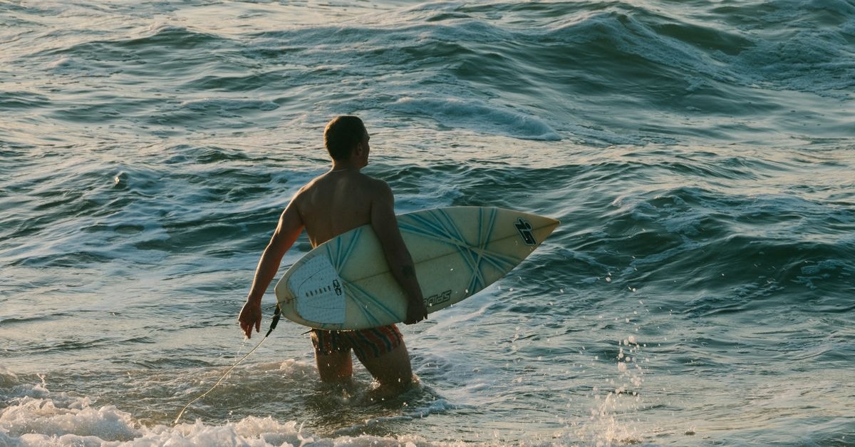 Wanning Travel Guide: Surf Culture, Slow Days on Hainan's Coast A surfer enters the ocean at Ballito Beach, KwaZulu-Natal, South Africa during the day.