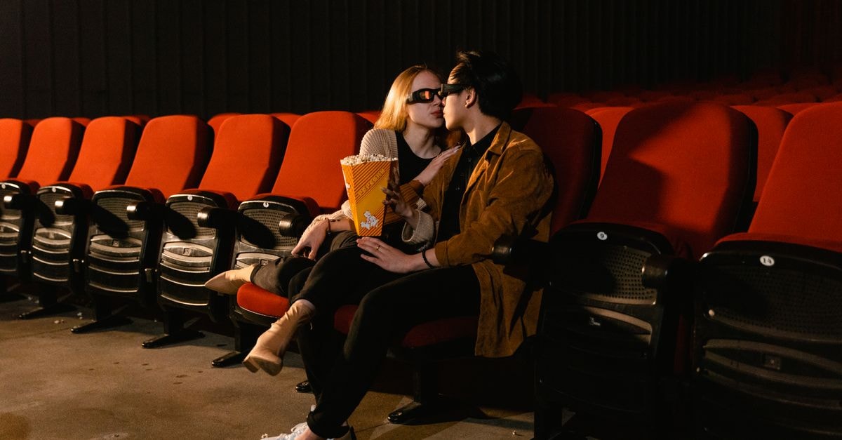 Couple wearing 3D glasses sharing popcorn in a cozy movie theater setting.