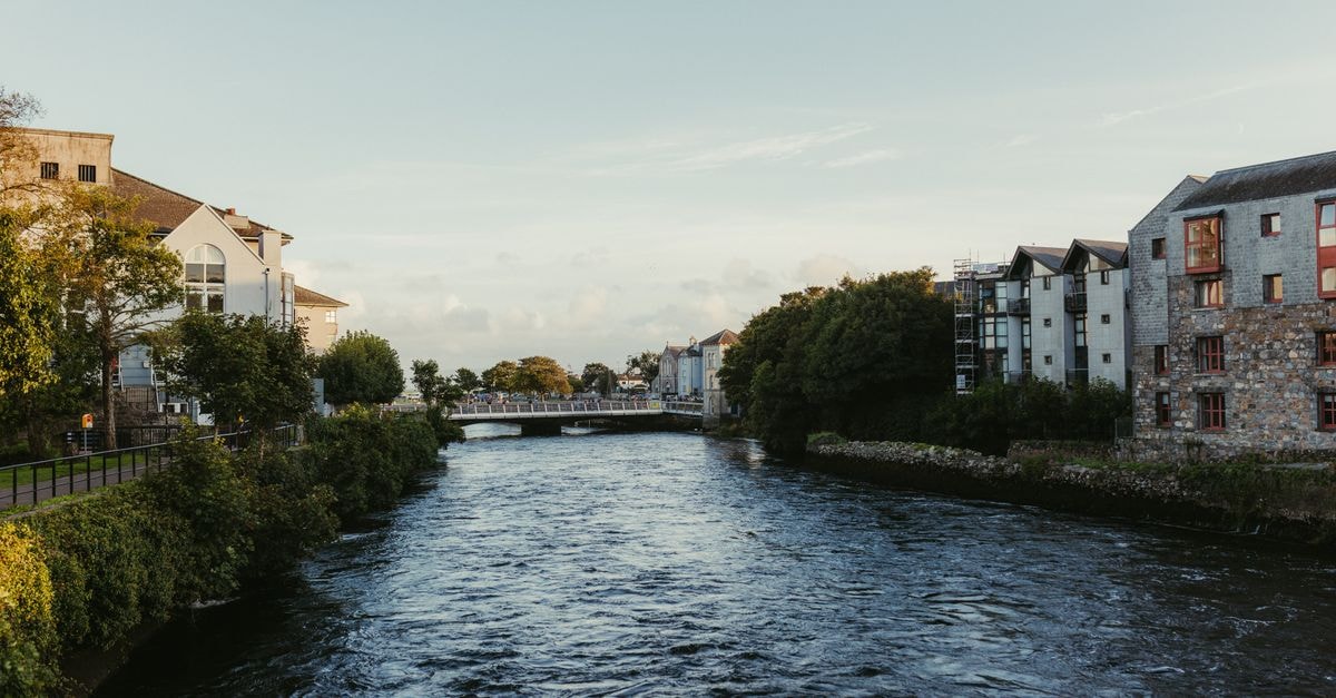 Galway Travel Guide: West of Ireland Charm Tranquil river scene in Galway with historic stone buildings and lush greenery at sunset.