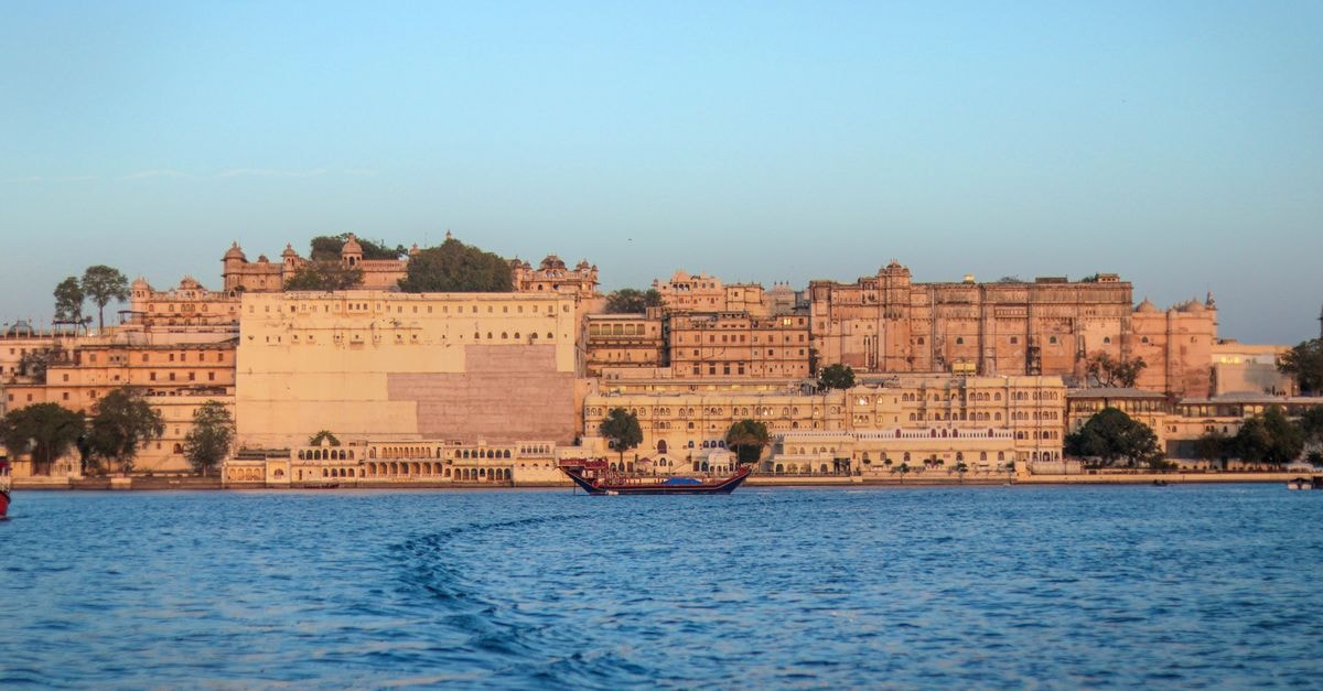 Udaipur travel guide: a calm lake city for first-time visitors View of the historic Udaipur City Palace in Rajasthan, India, across Lake Pichola during sunset.