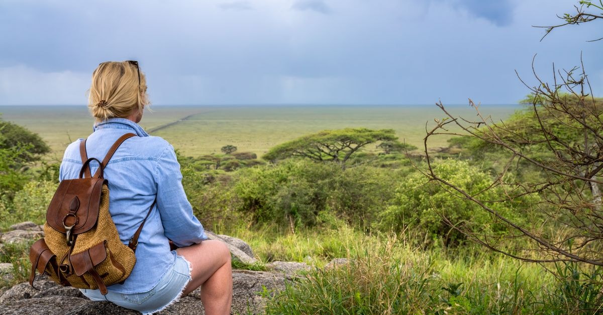 Njombe travel guide: a slow discovery in Tanzania's southern highlands Blonde woman with backpack enjoying view of expansive African landscape under overcast skies.