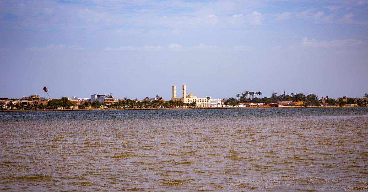 Hôtel de Djibouti in Djibouti: A Corner on Avenue Cheik Houmed Scenic riverside view of a town with palm trees under a clear blue sky, serene and tranquil.
