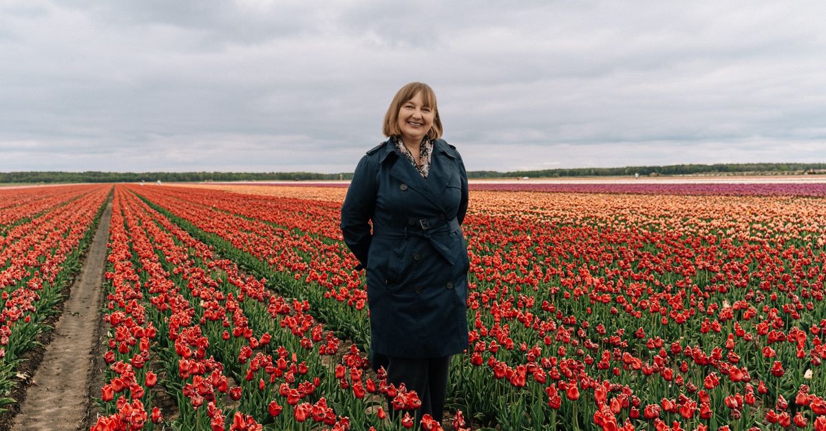 TULIP Hotels & Residences – Zwolle: Where a Hanseate Moat Becomes a Lobby Smiling woman standing amidst bright tulip fields in Tyszkowicze, Belarus on a cloudy day.