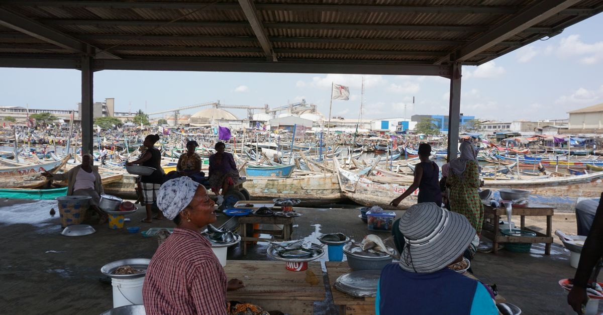 Women at Tema fish market in Ghana, bustling with boats and local vendors.