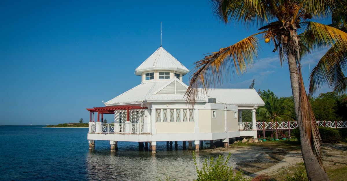 Bodden Town Travel Guide: Planning Tips, Costs and Things to Do Charming white building by the coast with palm trees, under a clear blue sky.