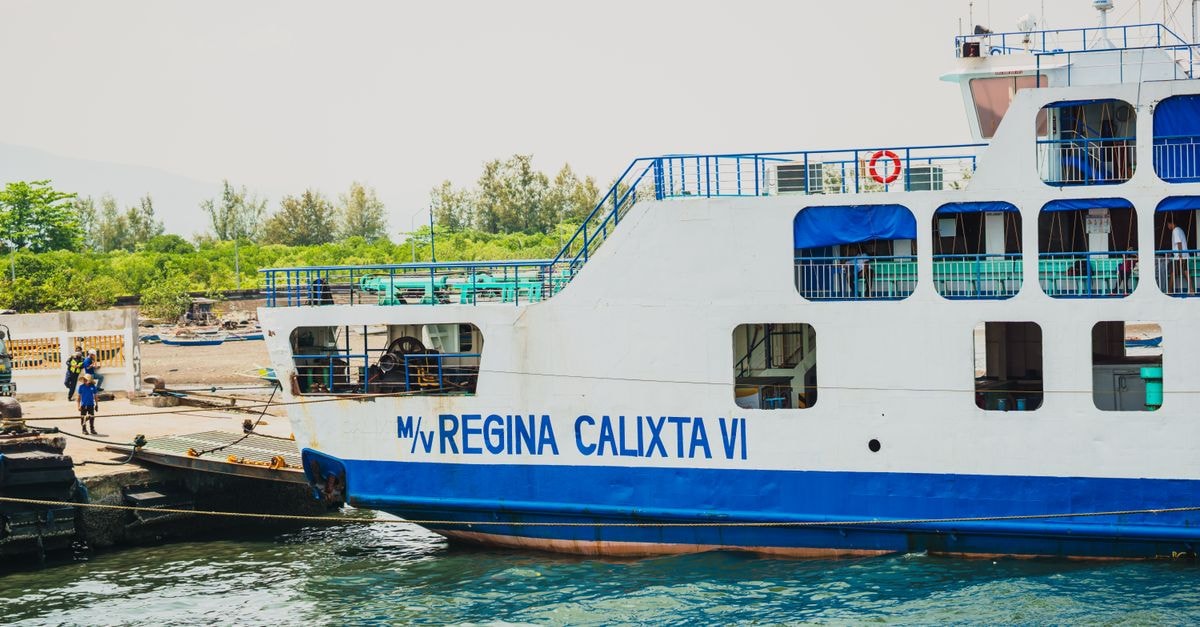 White and blue ferry 'Regina Calixta VI' docked at a picturesque port.