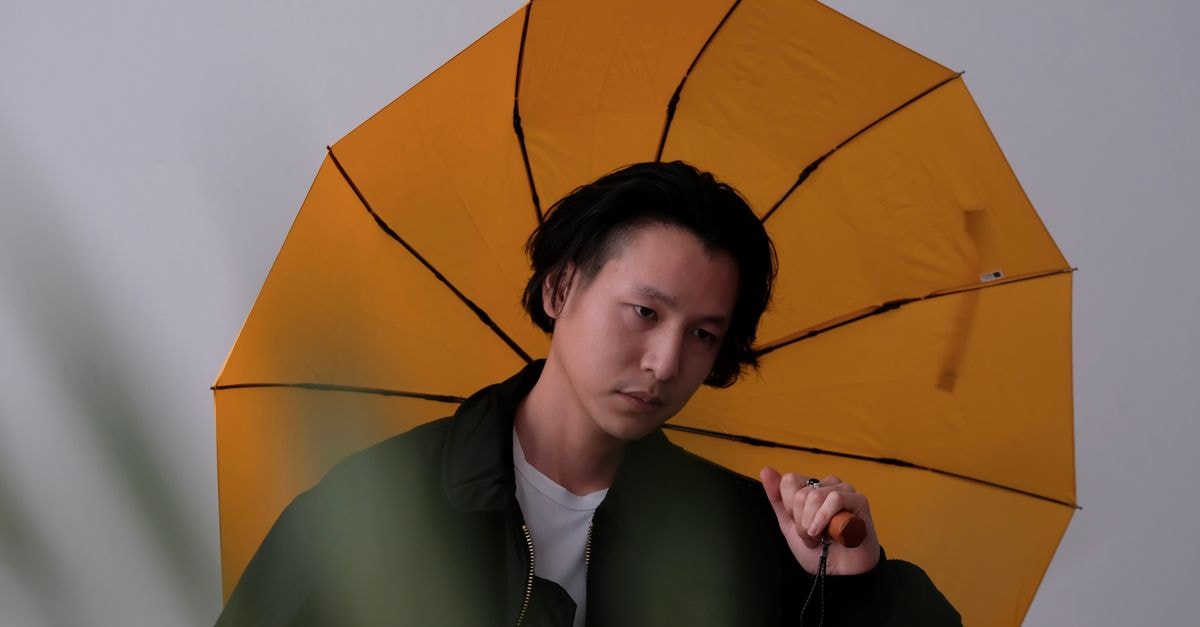 一位亞洲男性在攝影棚中撐著鮮黃色雨傘擺姿勢的肖像照。