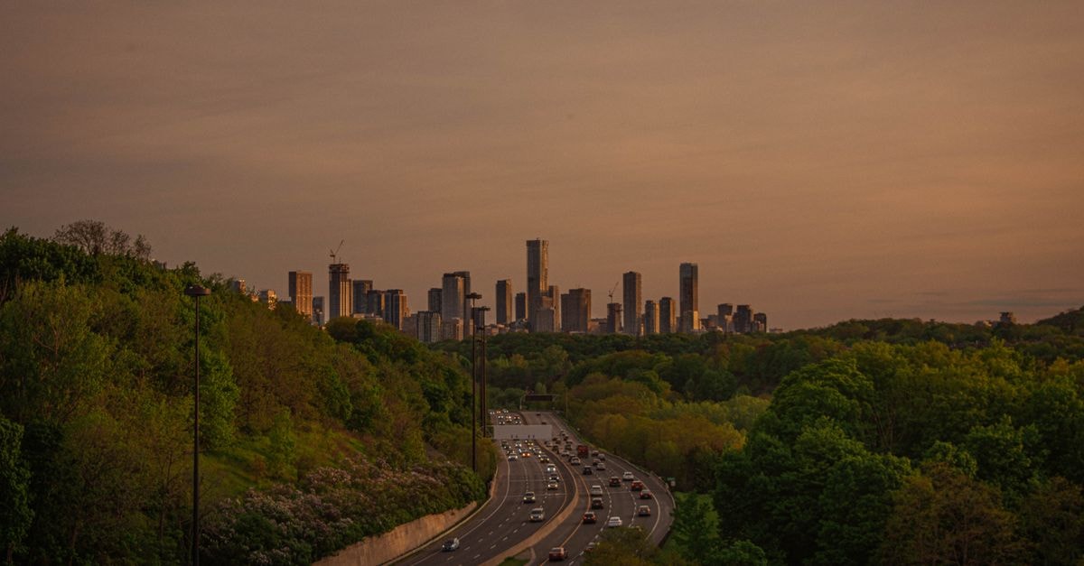 Quality Inn Airport West in Mississauga: Gateway to Pearson Aerial shot of city skyline with highway and forest during sunset.