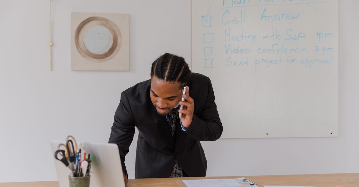 Businessman in an office making a call while working on a laptop with office supplies.