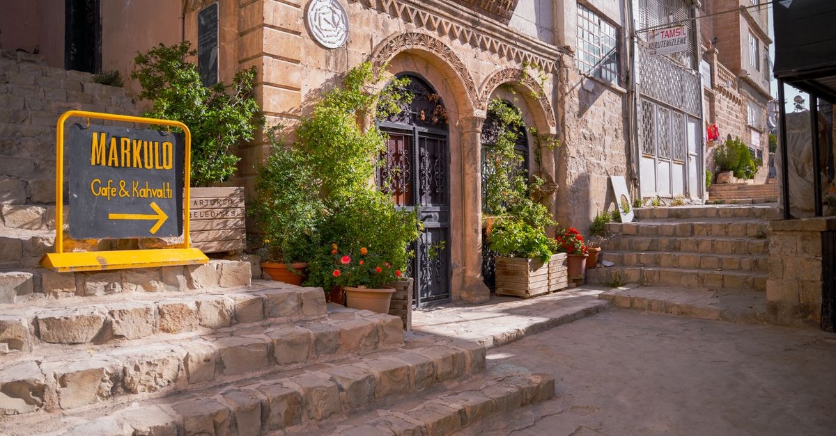 Merkezefendi Travel Guide: A Quiet District Worth a Slow Visit Cozy cafe entrance with stone steps and vibrant plants on a sunny day.
