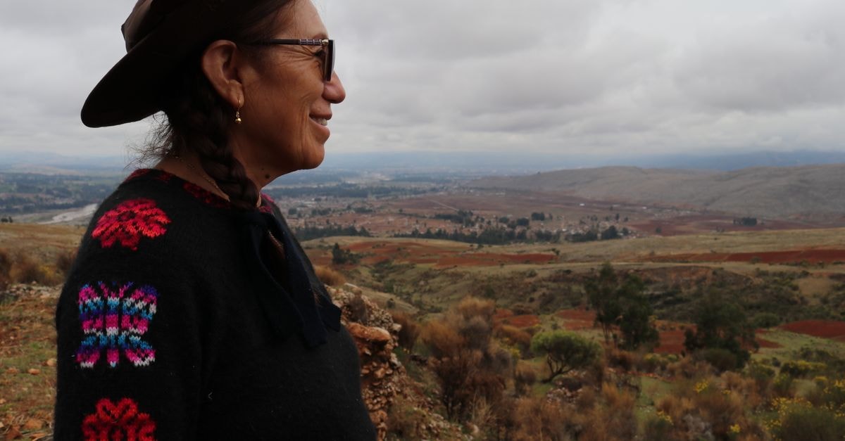 A woman in a hat and sweater admires the vast plains of Huancayo, Peru in a scenic landscape shot.