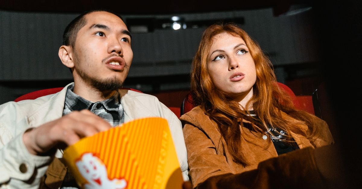 A couple sits in a movie theater, engrossed in a film while enjoying popcorn.