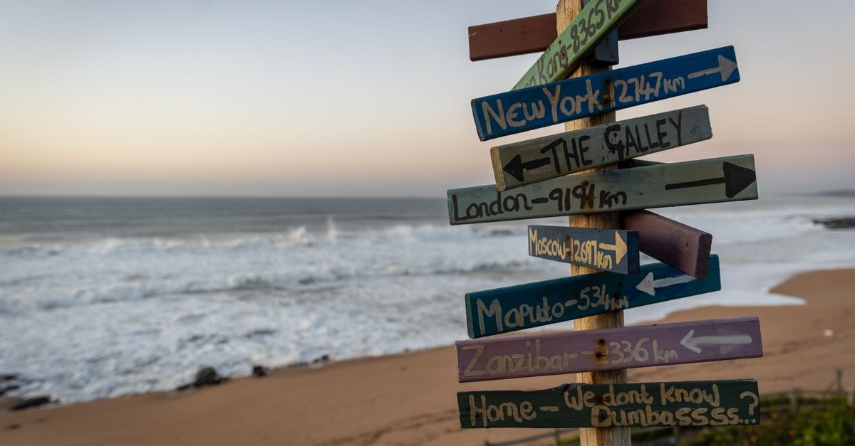 Boma Travel Guide: Planning Tips, Costs and Things to Do A vibrant signpost with city names at a beach on Dolphin Coast, South Africa.