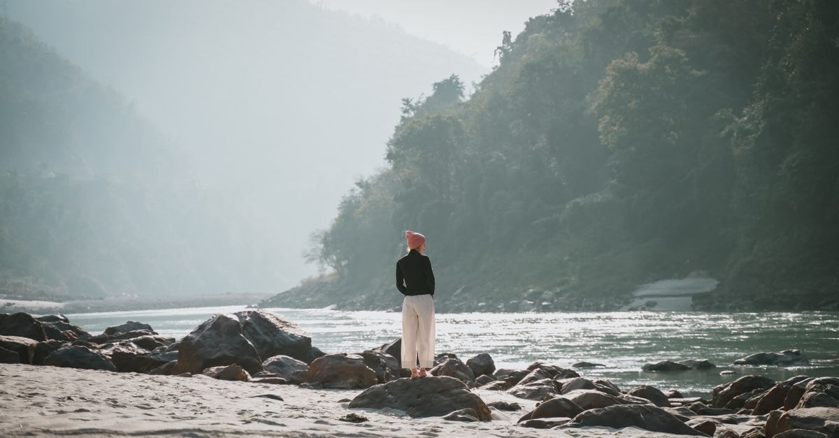 Avdhoot Ashram, Rishikesh — A Spiritual Address on Hira Lal Road A woman stands by the scenic river in Rishikesh, India, surrounded by mountains.