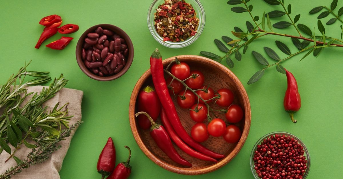Top view of chilies, cherry tomatoes, beans, and herbs on green background. A colorful culinary arrangement.