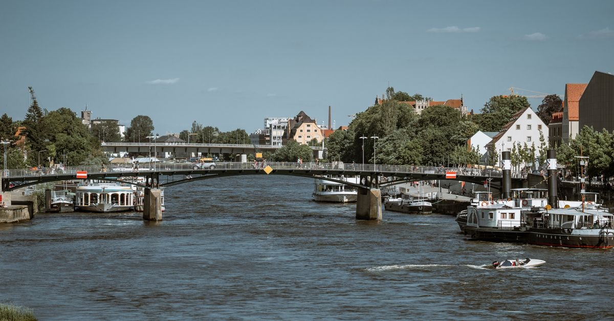 Charming riverside scene of boats and bridge in Regensburg, Germany.