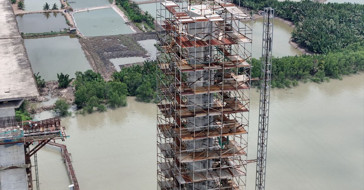 Vietnam's Dak Nong plant produces first aluminum ingots; Jamaica projects 24% bauxite-alumina earnings rise Aerial shot of construction scaffolding by a river, surrounded by lush greenery.