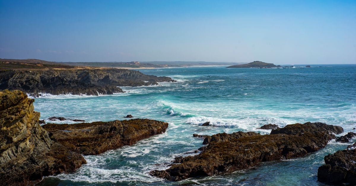 Setúbal Travel Guide: Arrábida Adventures Made Simple Beautiful rocky coastline in Setubal, Portugal with waves crashing against the shore under a clear blue sky.