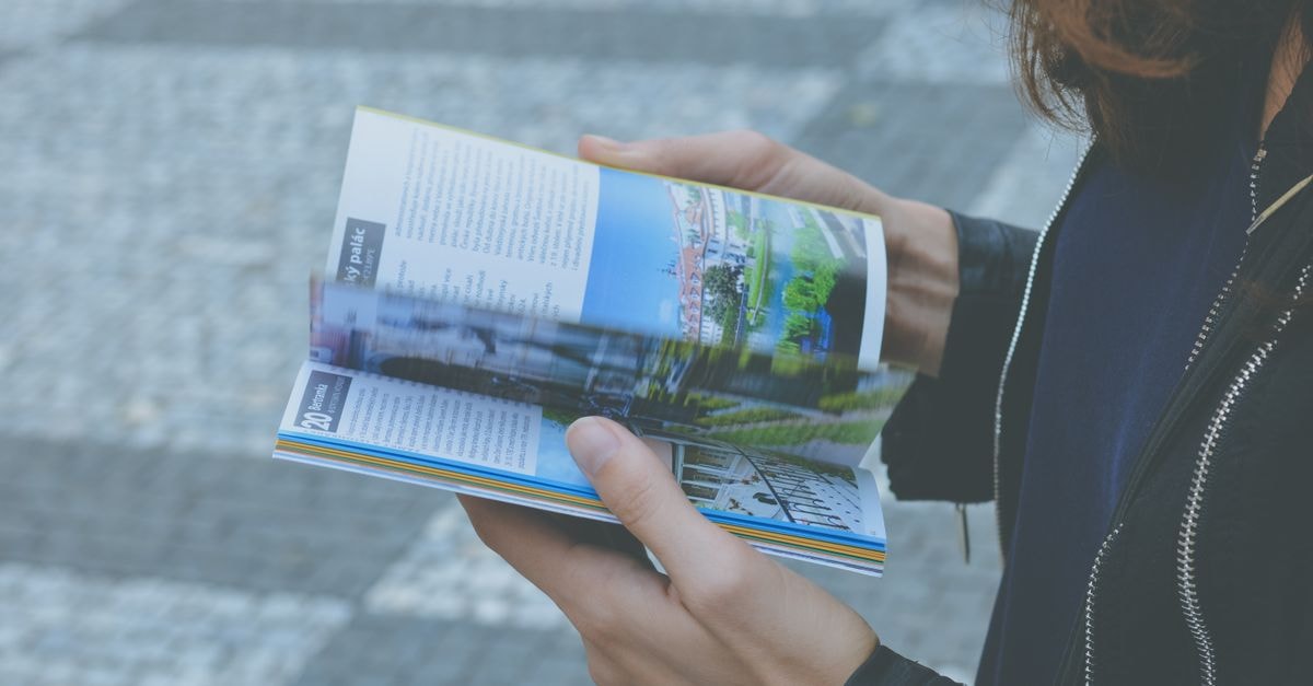 A person flipping through a travel book outdoors, showcasing a variety of vibrant pages.