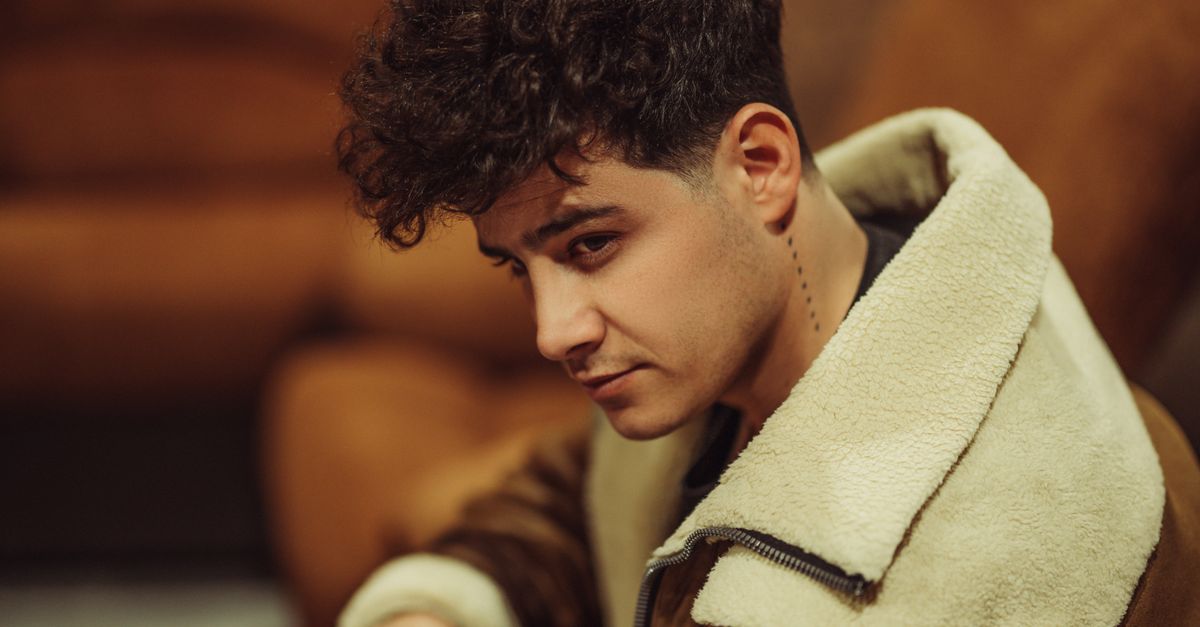 Sanremo 2027: De Martino begins song selection with trimmed Big lineup Model with curly hair poses in a fashionable shearling jacket indoors.