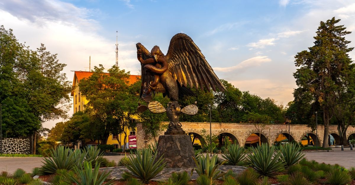 A grand eagle sculpture decorates a plaza in Ciudad de México, surrounded by lush greenery.