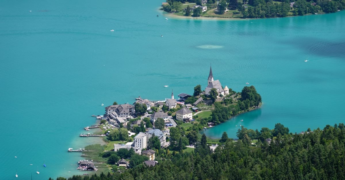 Klagenfurt Travel Guide: Lakeside Charm in Austria's South Stunning aerial view of a picturesque village nestled on a turquoise lake, surrounded by lush greenery.