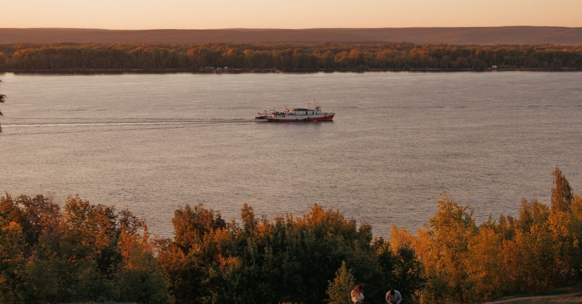 A tranquil river scene showing a boat sailing at sunset with lush greenery in the foreground.