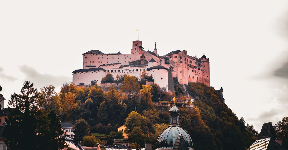 Salzburg Travel Guide for July 2026: Festival Season, Summer Traffic Rules & Budget Tips View of the Hohensalzburg Fortress atop a hill surrounded by vibrant autumn foliage in Salzburg, Austria.