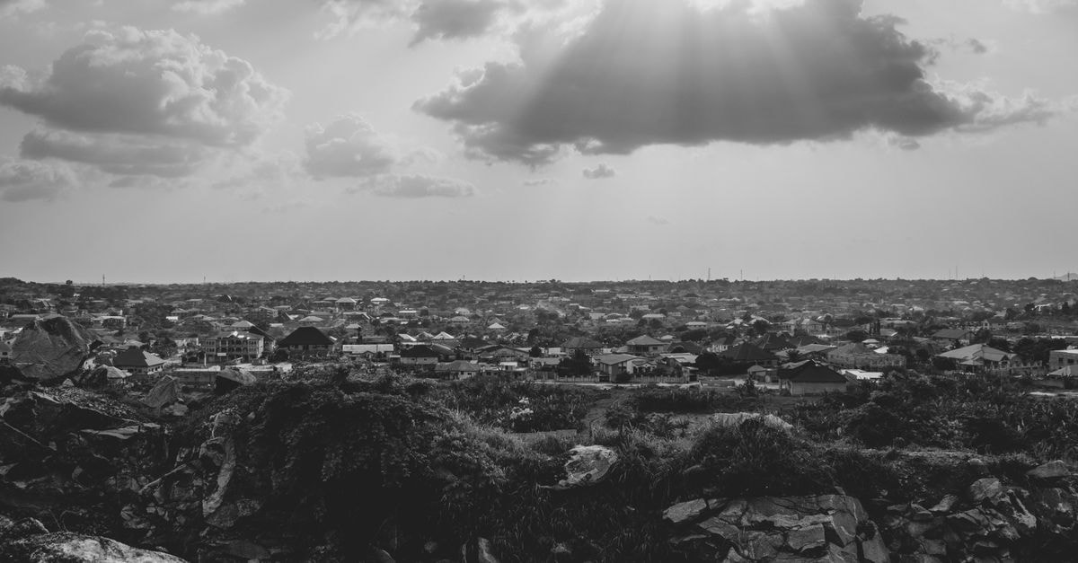 Gab Hotel, Kano — Ibrahim Taiwo Road Stop on a Busy City Stretch A captivating black and white cityscape showing sun rays breaking through clouds over urban buildings.