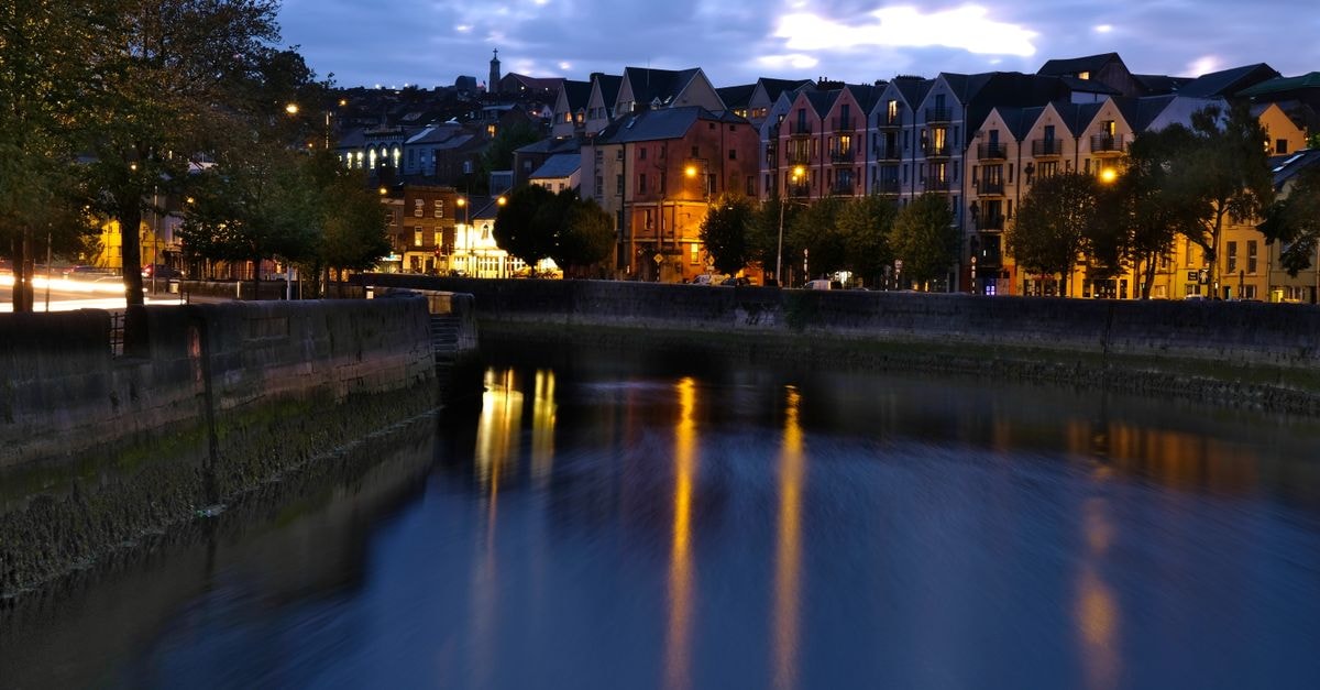 Nighttime view of Cork city's illuminated canal and buildings, reflecting lights beautifully.