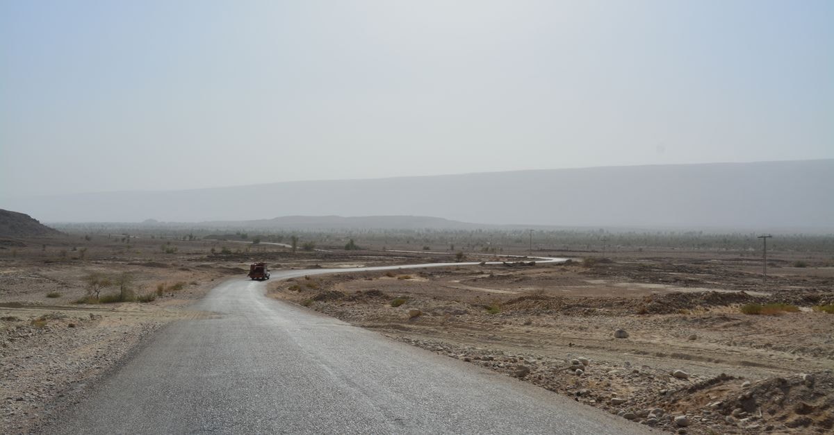 Khamis Mushait Travel Guide: Roads, Buses, and Mountain Days A solitary road winds through an expansive desert under a hazy sky.
