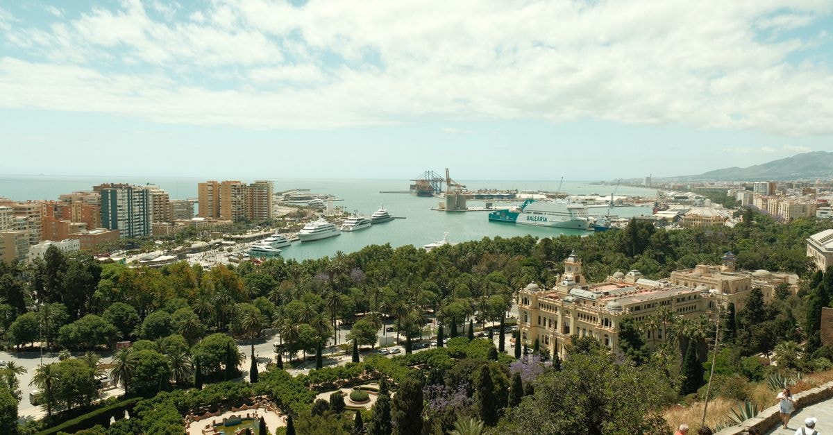 Woodbrook on the Avenue, Port of Spain — A Gated Boutique Stay Off Ariapita Aerial view of Malaga's harbor, lush gardens, and city buildings under a blue sky.