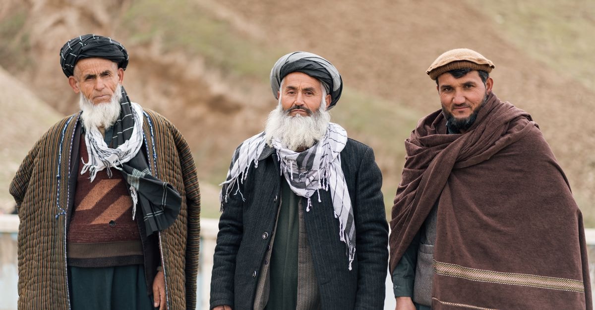 Three Afghan men in traditional attire standing outdoors, showcasing cultural attire and identity.