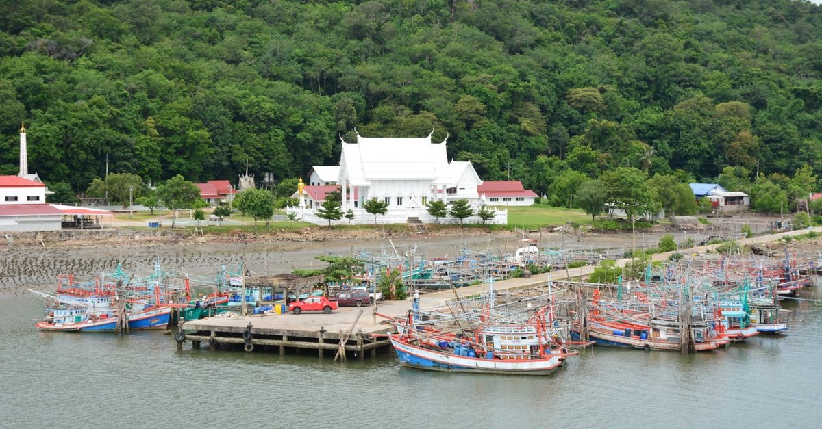 Colorful fishing boats docked with a temple in the background in Chanthaburi, Thailand.
