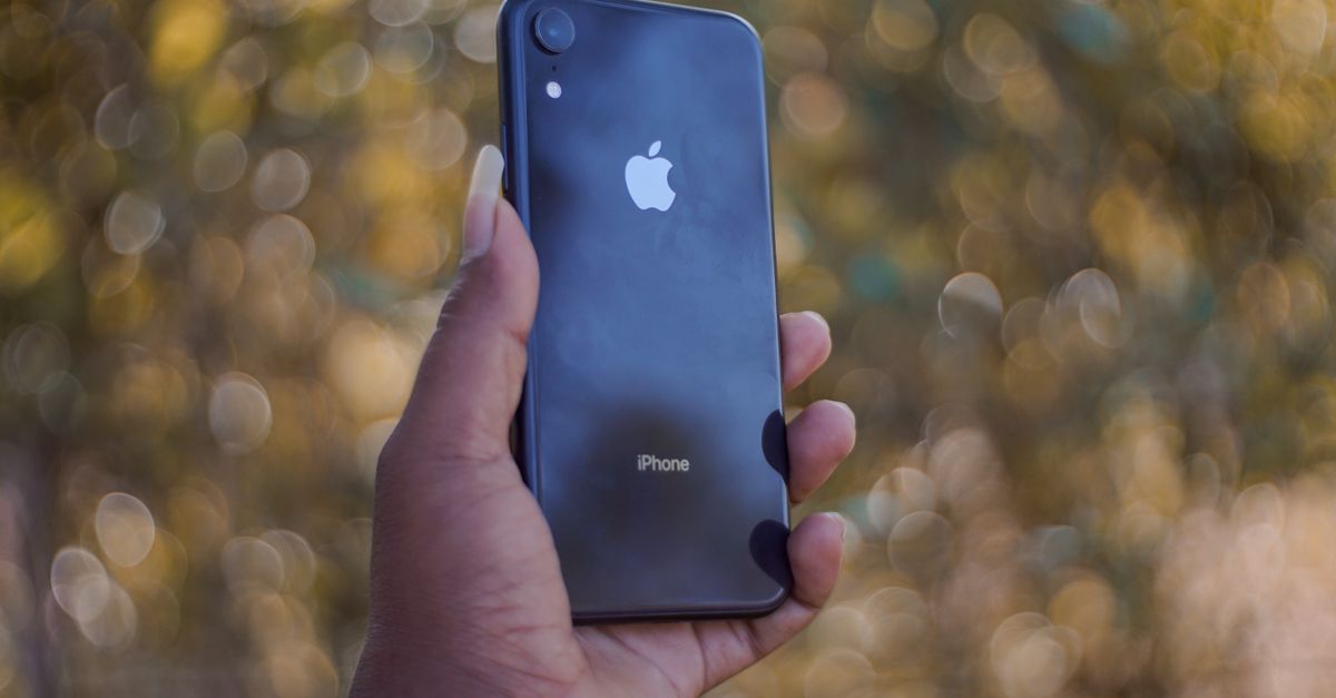 Apple lines up July 28 US leasing launch, UK AppleCare One rollout and iPhone 18 display talks A close-up of a hand holding a smartphone with a blurred outdoor background.